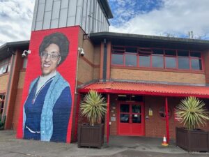 Mount Stuart Primary School, external view. Features a large painted mural of a Black woman, she is wearing a blue top and glasses, and is smiling. 