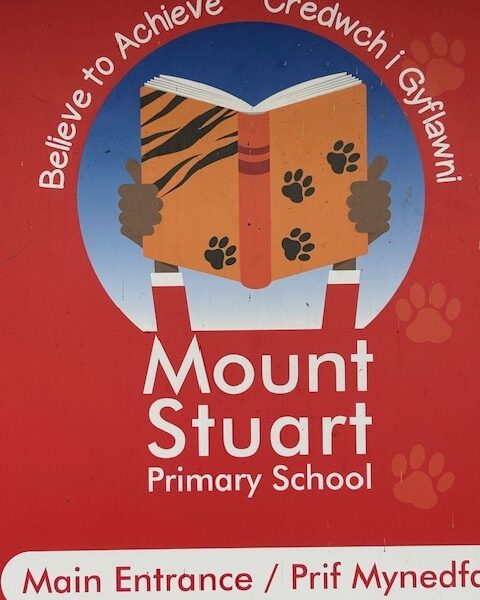 Mount Stuart Primary School moto, Believe to Achieve/Credwch i Gyflawni. The logo is two brown hands holding up an orange book against a blue sky and red background.